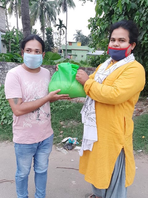 A photograph of two people standing outside holding a green bag
